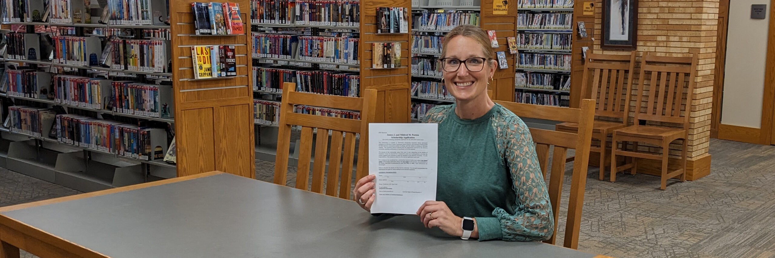 Librarian sitting at a table holding a Postma Scholarship application form